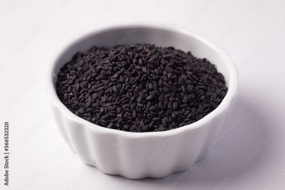Black sesame seeds in a white ceramic cup on a white background Black sesame seeds in a white ceramic cup on a white background