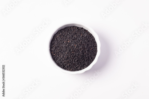Black sesame seeds in a white ceramic cup on a white background