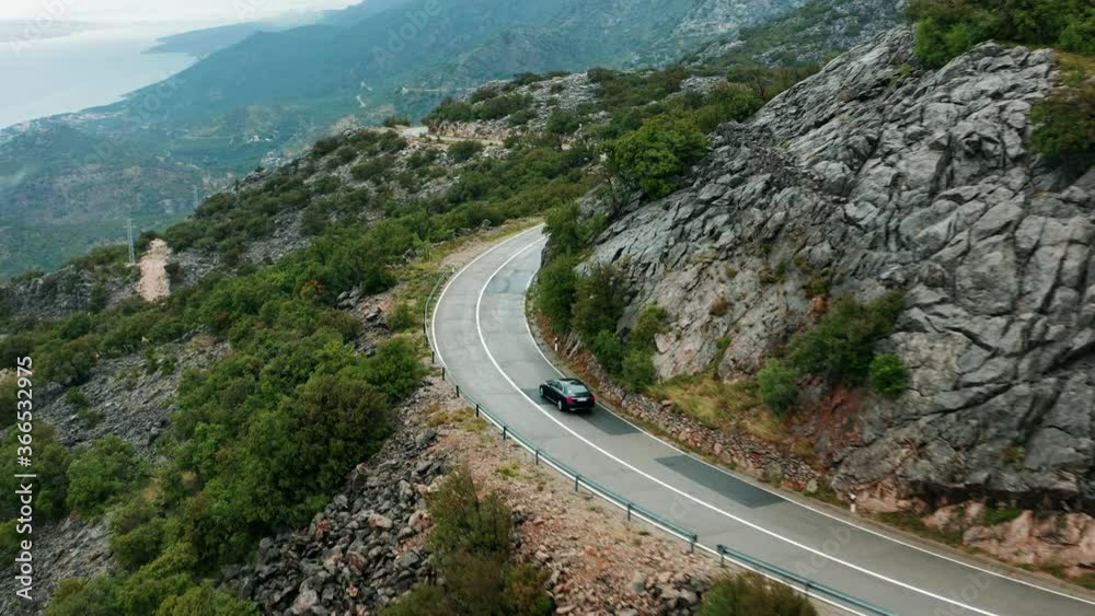 Mountain road of Velebit in Croatia, Aerial as black car travels around mysterious bend Mountain road of Velebit in Croatia, Aerial as black car travels around mysterious bend