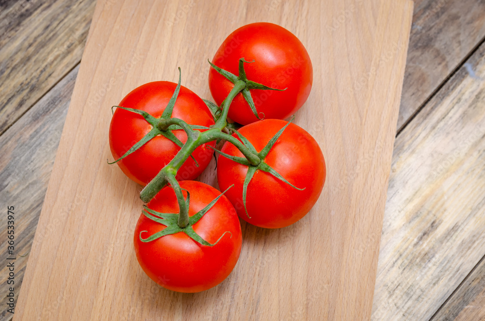 Fresh, ripe, juicy, red tomatoes on a branch close-up on a wooden stick on the table, view top Fresh, ripe, juicy, red tomatoes on a branch close-up on a wooden stick on the table, view top