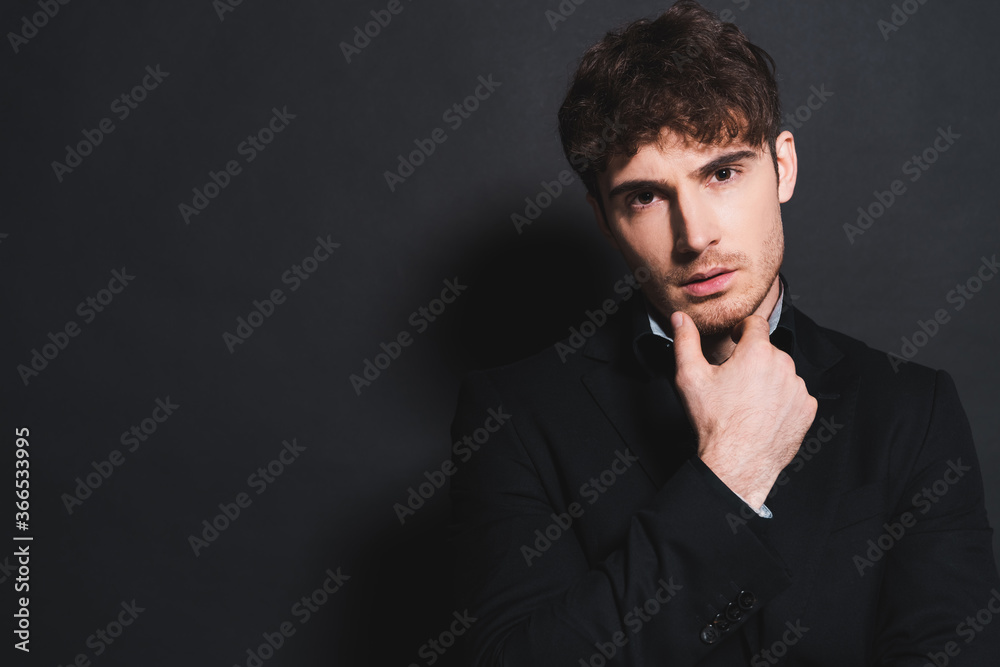 handsome man in formal wear looking at camera and touching face on black