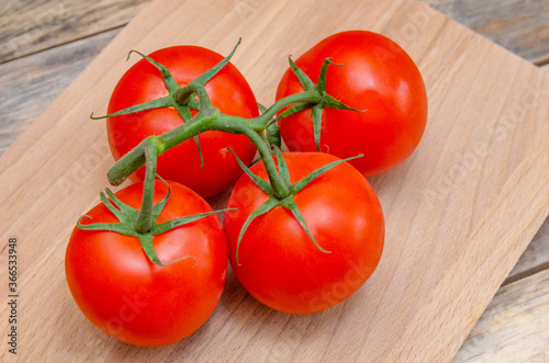 Fresh, ripe, juicy, red tomatoes on a branch close-up on a wooden stick on the table