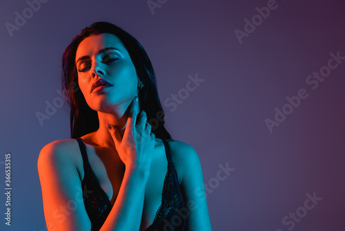 sexy young woman with closed eyes touching neck isolated on purple