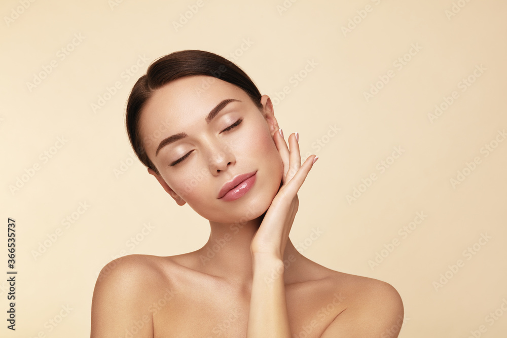 Softness. Beauty spa model closed eyes and touching her face against beige background. Softness. Beauty spa model closed eyes and touching her face against beige background.