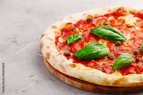 pepperoni pizza with capers and basil closeup on light concrete or stone table or background