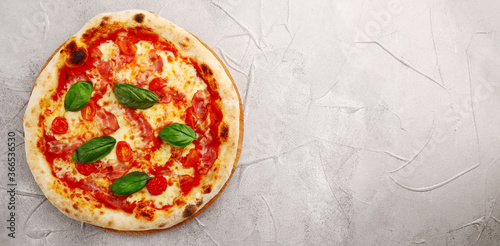 pizza with bacon, cherry tomatoes and basil on light concrete or stone table top view banner