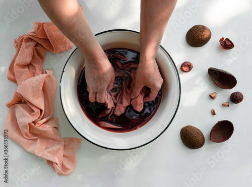 Woman's hand soaking fabric in pot with natural avocado dye, top view photo