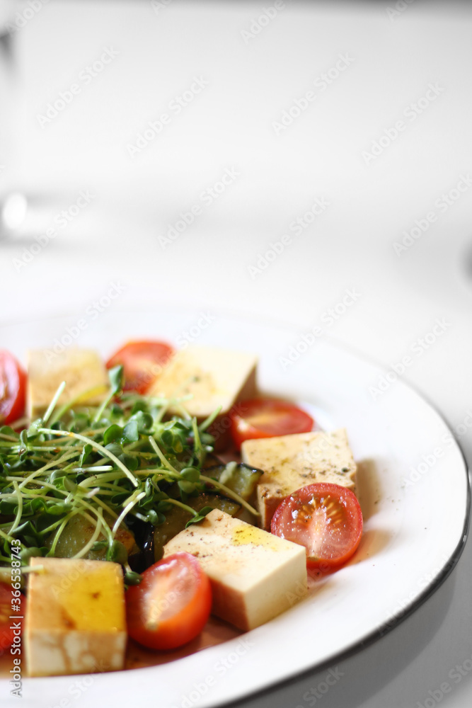 veggie salad with tofu, microgreen and cherry tomatoes close up on white table