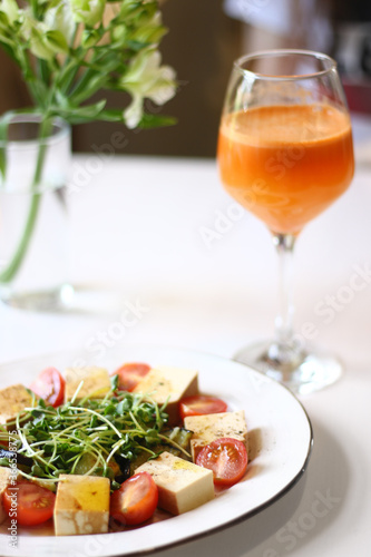 veggie salad with tofu  microgreen and cherry tomatoes and glass of carrot juice on white table
