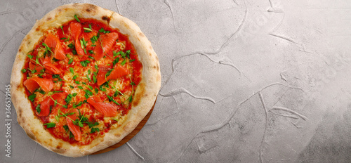 salmon pizza with green banner on gray concrete or stone table top view.
