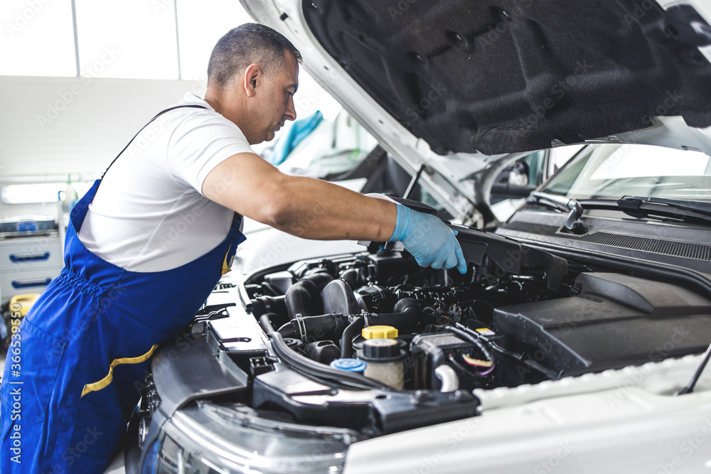 Car service mechanic worker standing in front of car engine open hood and working Car service mechanic worker standing in front of car engine open hood and working