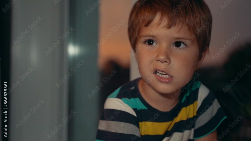 the boy sits by the window and wriggs. Outside the window evening the boy sits by the window and wriggs. Outside the window evening