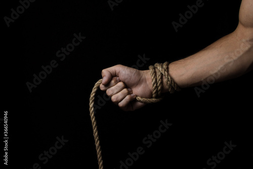 Male hand holds a rope on a black background. Jute rope wraps around the arm.