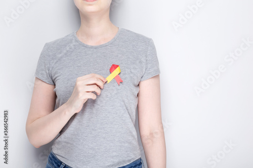 World Hepatitis Day concept. Girl in gray T-shirt holds in her hand awareness symbol red-yellow ribbon. Gray background. Copy space photo