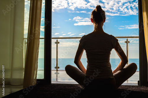 The beautiful woman practicing yoga on a exercise mat and sitting Assana Yoga Pose on a balcony with the seascape view.