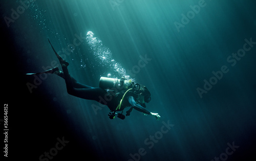 Underwater view of diver wearing wetsuit, diving goggles and oxygen cylinder, air bubbles rising.