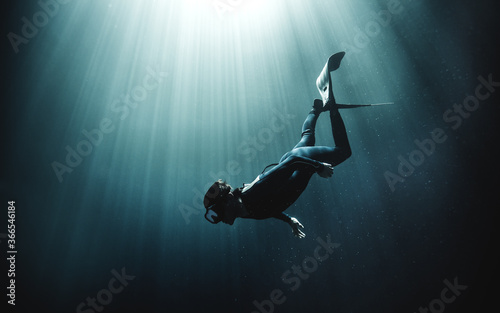 Underwater view of diver wearing wet suit and flippers, sunlight filtering through from above.