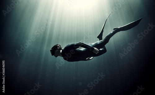 Underwater view of diver wearing wet suit and flippers, sunlight filtering through from above. photo
