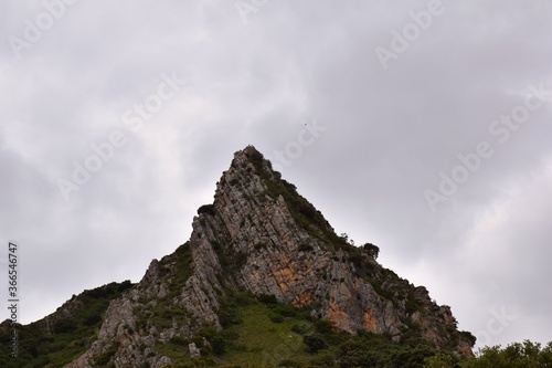 Small peak in the bush with well-defined vertical layers. Peg. Cloudy sky.