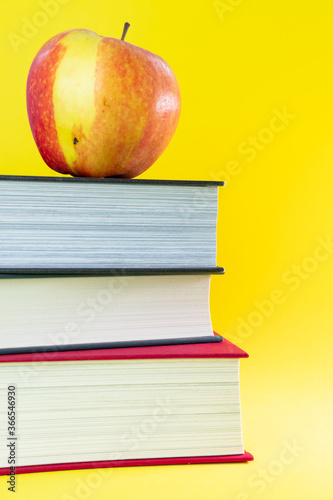 Pile of books witn an apple on the top in yellow background. Back to the school. Copy space.