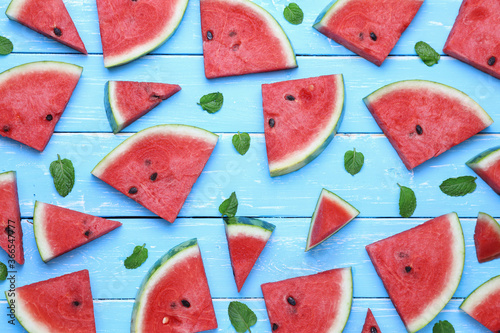 Top view, sliced watermelon fruit with many mints leaves on the old blue wooden table for background.