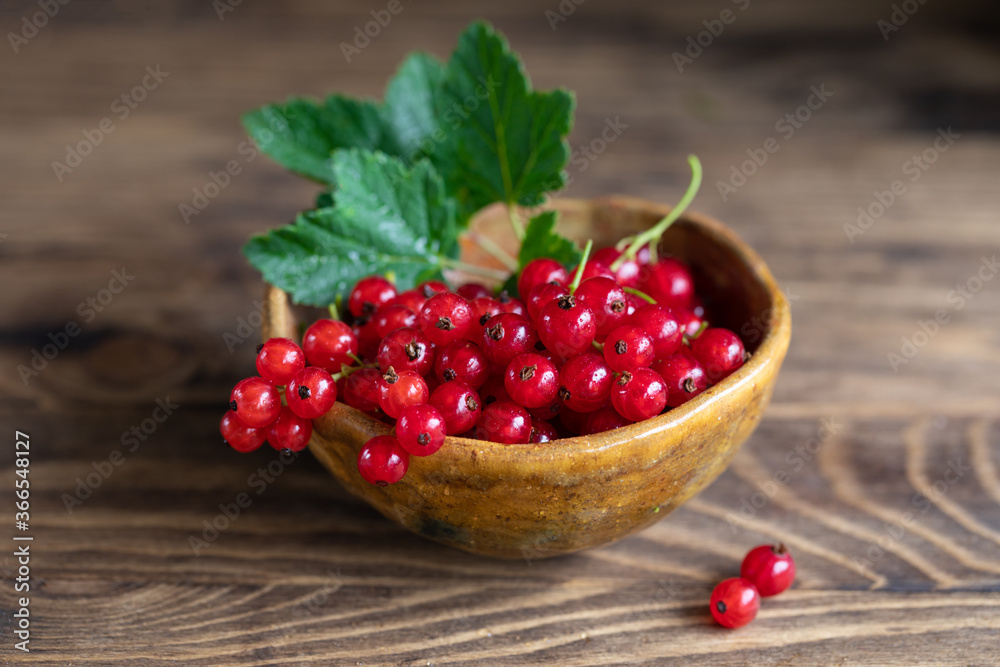 Red currant with leaves in bowl on rustic wooden table Red currant with leaves in bowl on rustic wooden table