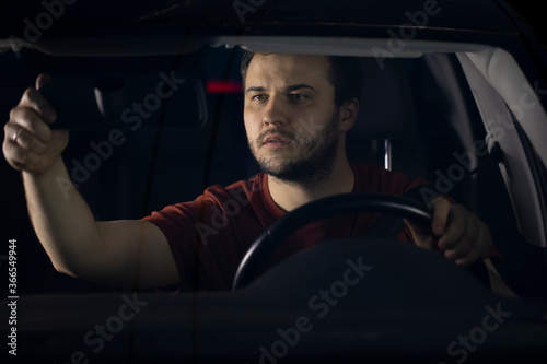 A handsome bearded man adjusts the rear view mirror before starting to move. Responsible driver, safe driving. Preparing the car for the trip.