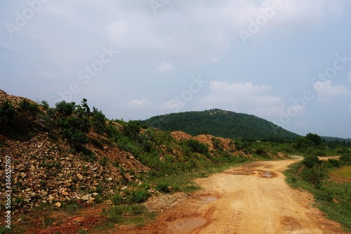 dirt  rural village road beside a small hillock in India.