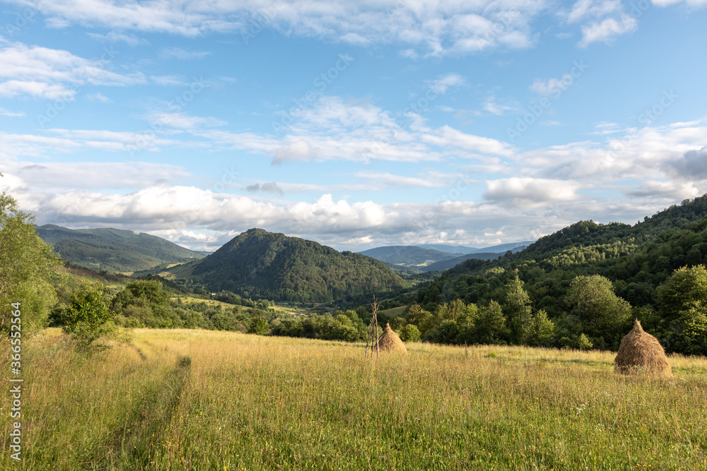 Panorama of the Carpathians with mountains, clouds, grass, haystacks and a field road