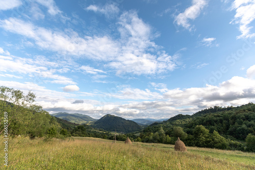 Panorama of the Carpathians with mountains, clouds, grass, haystacks and a field road