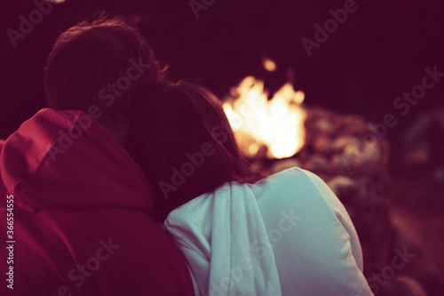 Portrait of a loving married couple sitting by the fire in nature. A man hugs a woman, view from the back. Rest in the country with a camper. Family holidays away from city noise. Toned sepia