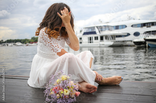 the bride is sitting barefoot on the pier of the yacht club