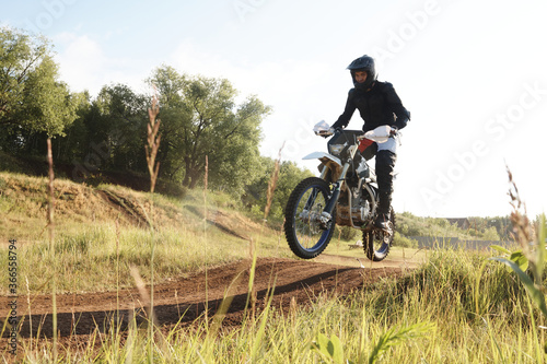 Extreme man in protective wear being in mid air while riding motorbike on hills at competition