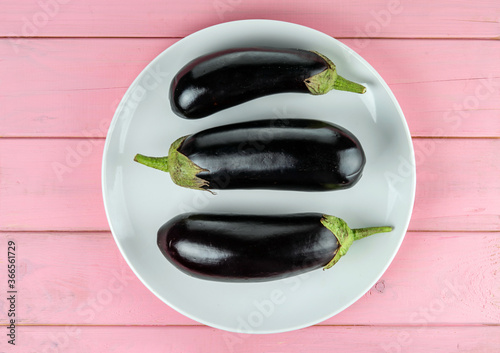 Long purple eggplants lie on a white plate on a pink background. photo