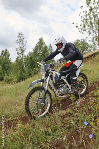 Focused man in helmet getting weight back while riding motorcycle downhill