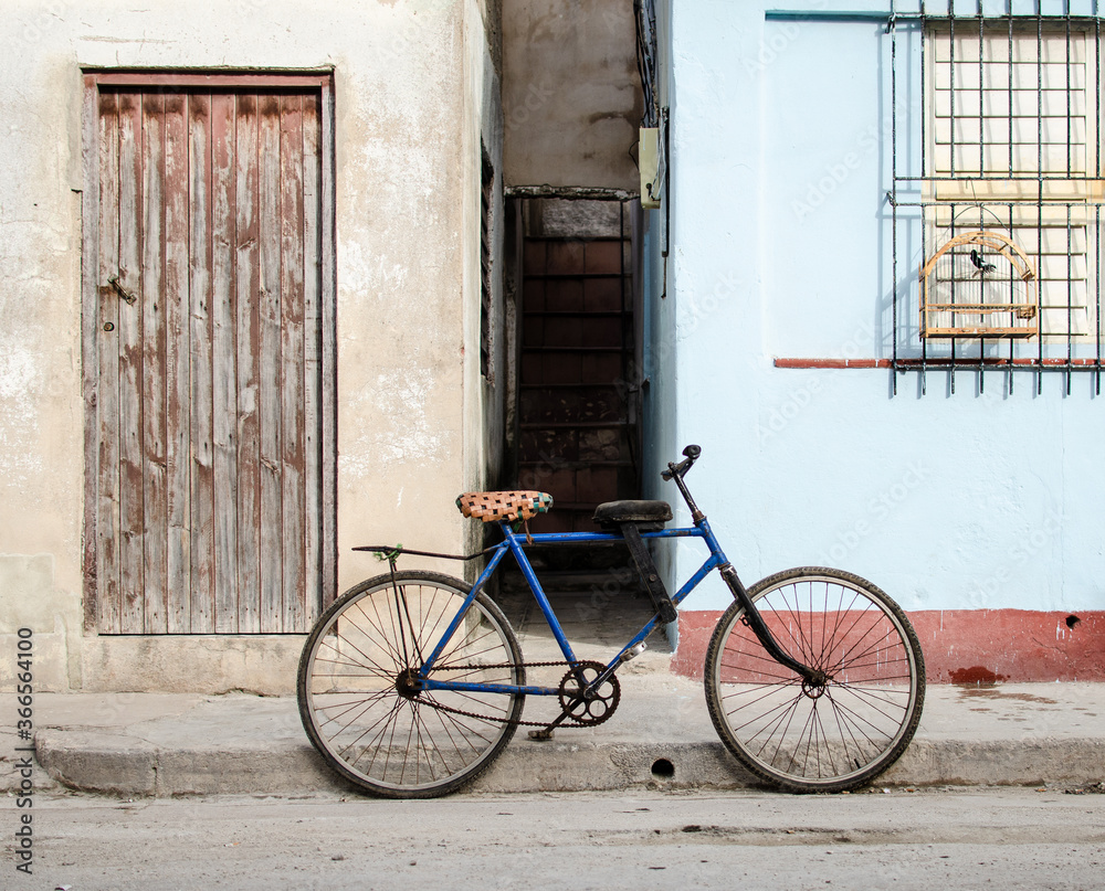  Blue bike bicycle in front of Cuban house with singing bird in cage, red and light blue facade, wooden door and window