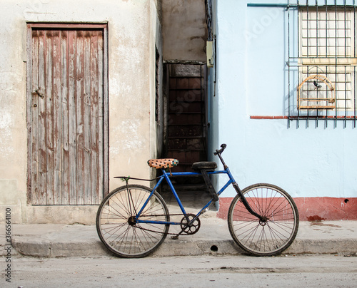  Blue bike bicycle in front of Cuban house with singing bird in cage, red and light blue facade, wooden door and window