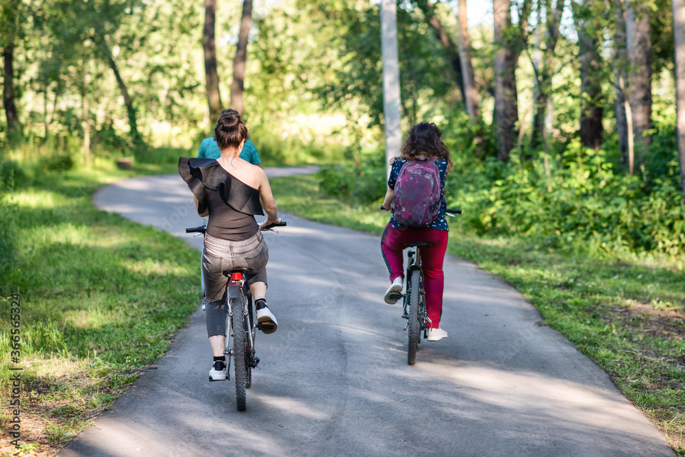 Two girl friends riding their bicycles in a park in summer in the sunny morning. Two girl friends riding their bicycles in a park in summer in the sunny morning.