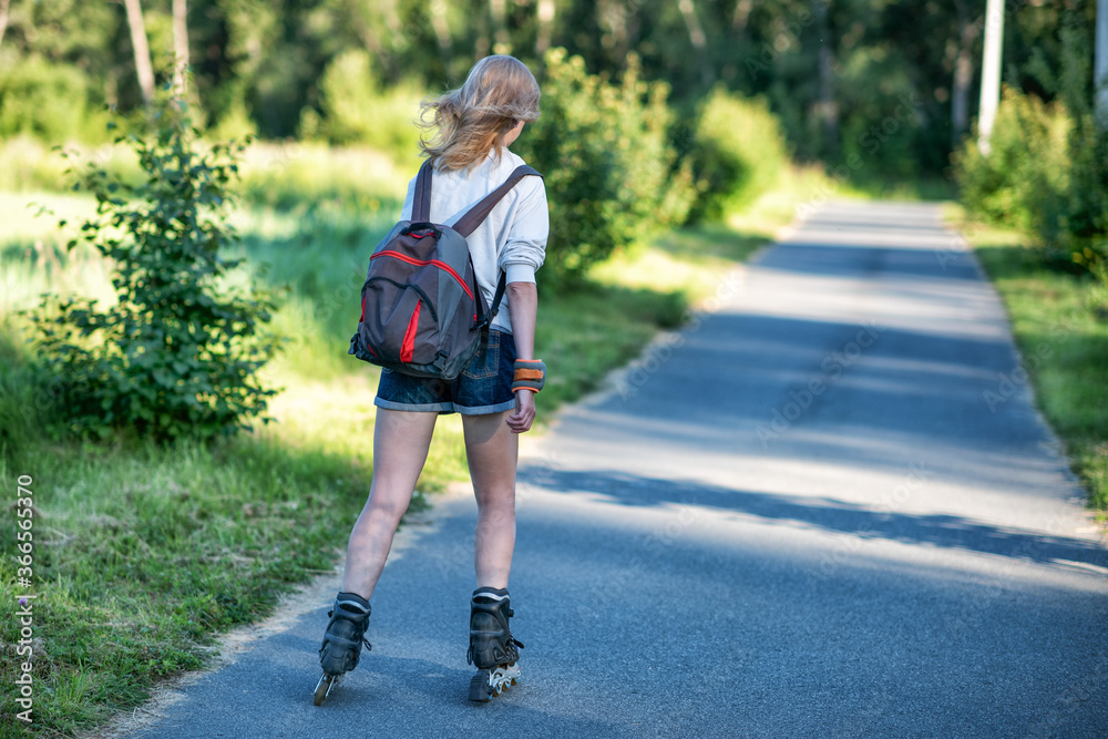 Sporting girl roller skating in a park on summer day.