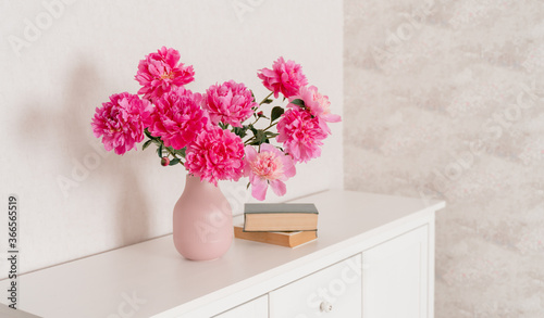 Fototapeta Naklejka Na Ścianę i Meble -  A large bouquet of peonies in a pink vase in a bright room on a white chest, books are nearby. fresh flowers at home, greenhouse, minimalist, cozy loft interior