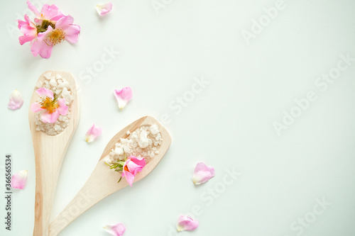 Bath salt in wooden spoons with flowers and rose petals, on a white background. The view from the top.