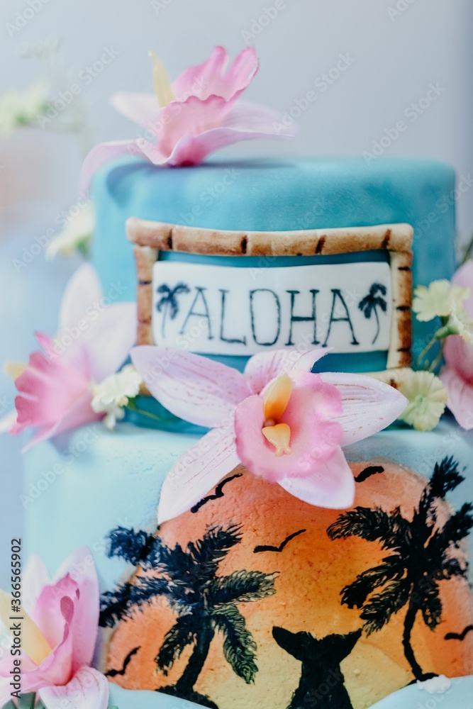 Vertical shot of a Hawaiian thematic cake decorated with pink flowers and 'aloha' text