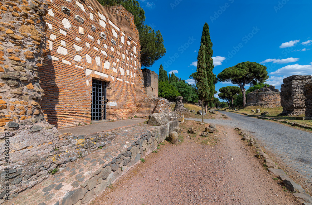 Perspective view of the brick tomb on the Via Appia Antica, Rome. The road was the most important of the Roman Empire, remains of other tombs, rich vegetation, maritime pines, cypresses.