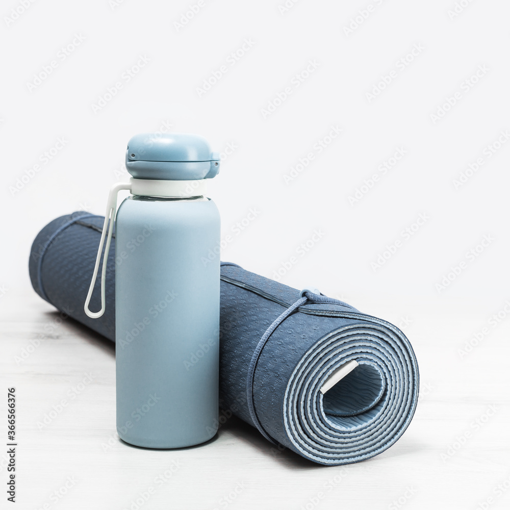 Rolled blue yoga mat and blue water bottle on grey wooden surface. Gender neutral fitness yoga and exercise concept with copy space. Active lifestyle. Workout at home or gym Rolled blue yoga mat and blue water bottle on grey wooden surface. Gender neutral fitness yoga and exercise concept with copy space. Active lifestyle. Workout at home or gym