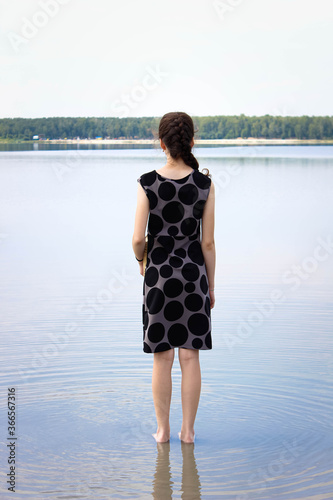 A teenage girl stands on the lake in a dress, feet in the water back. To enjoy the scenery.