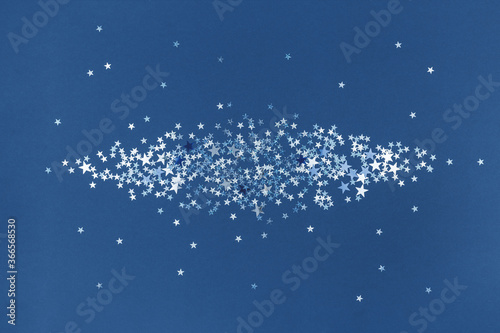 Blue scattered silver holographic glitter confetti star shaped on blue background. Flat lay top view copy space. Festive holiday pastel backdrop. Birthday, giveaway, Christmas, New Year. Overlay