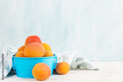 Fototapeta Naklejka Na Ścianę i Meble -  Juicy ripe apricots in a blue craft vase on a white table. Copy space.