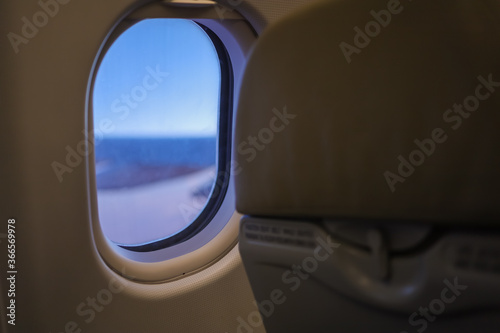 Close up of oval airplane window and back of economy seat with blue sky. transportation and Travel Concept.