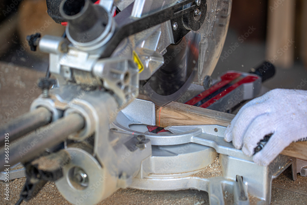 Fototapeta premium A carpenter cuts a timber beam with a circular saw. A closeup of hands in gloves. A sharp rotating disc that cuts through wood. Shavings and sawdust fly.