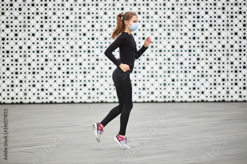 A young girl trains on the street in a black tracksuit. The white textured wall of the city building in the background. Empty space for your text.